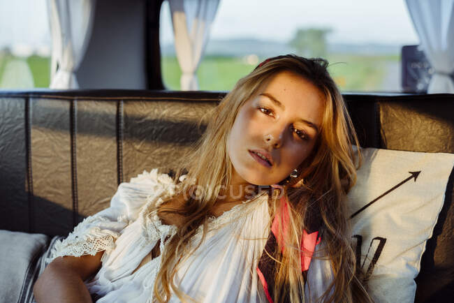 Привлекательная блондинка в винтажном фургоне, лежащая на сиденье в солнечный день и смотрящая в камеру — стоковое фото