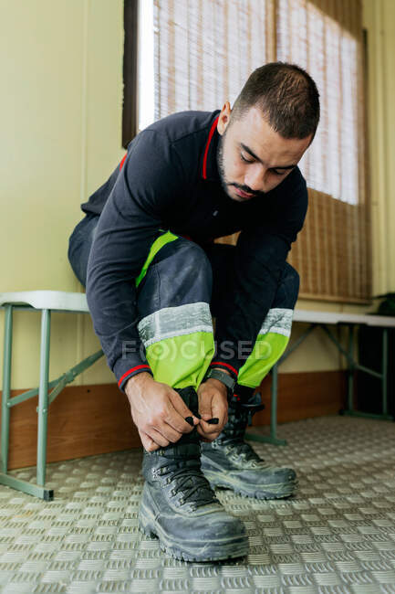 Seated firefighter buckling his boots before starting work in the metal-floored men's locker room — Stock Photo