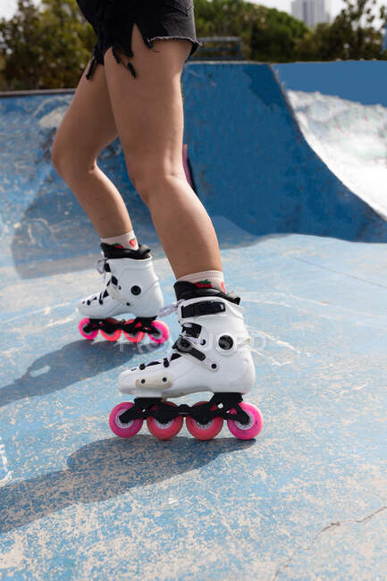 Обрізати анонімні жіночі ноги в білих роликових лезах з рожевими колесами, що стоять на бетонній тротуарі в скейт-парку — стокове фото