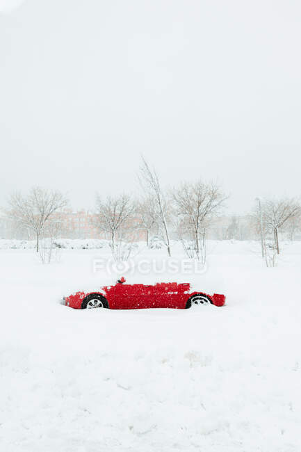 Carro vermelho sob snowdrift entre árvores sem folhas durante a queda de neve no dia de inverno nublado em Madrid — Fotografia de Stock