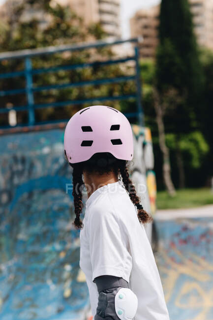 Young African American female in eyeglasses wearing light lilac protective helmet and gray elbow pads skating in park — Stock Photo
