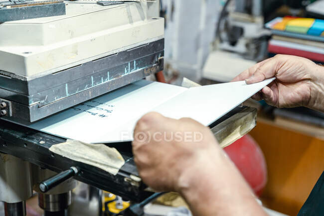 Crop unrecognizable artisan putting papers into aged printing press machine during work in studio — Stock Photo