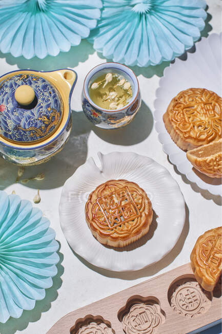 D'en haut de mooncakes traditionnels avec remplissage servi sur la table avec des moules de cuisson près de la bouilloire avec tisane dans la pièce lumineuse — Photo de stock