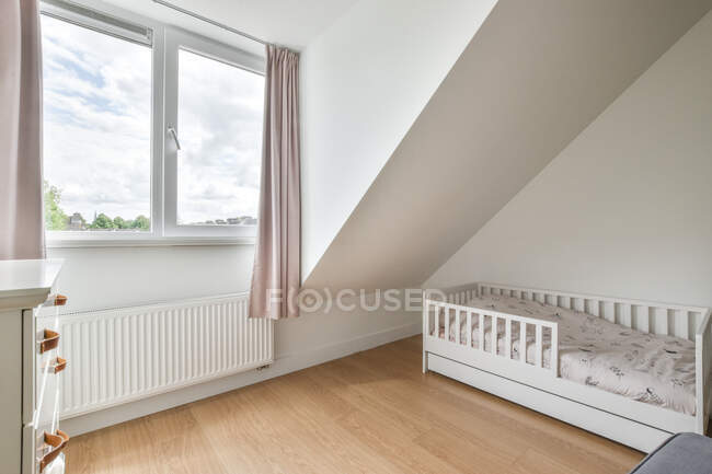 Детская кровать в светлой просторной спальне с занавеской на окне в квартире — стоковое фото