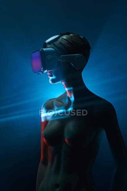 Dummy of woman in futuristic VR goggles placed under bright projection in dim room — Stock Photo