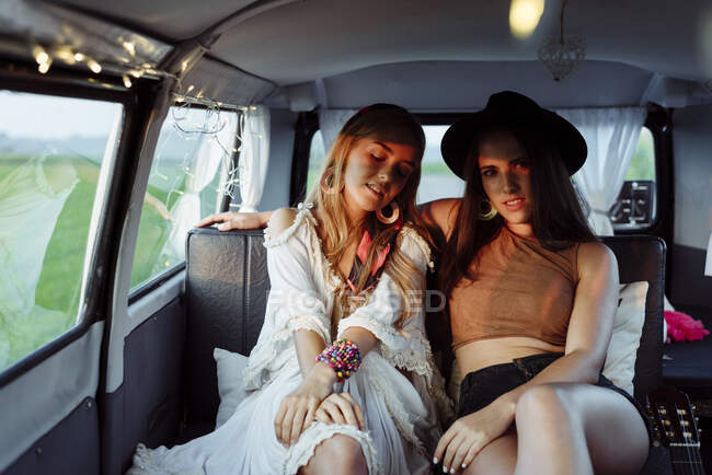 Duas lindas garotas caucasianas deitadas no assento dentro de uma van vintage olhando para a câmera — Fotografia de Stock