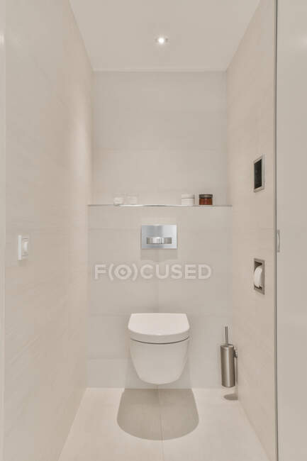 Contemporary bathroom interior with toilet bowl between beige ceramic walls in house with glowing lamp — Stock Photo