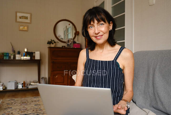 Счастливая женщина, сидящая на диване и работающая дома на ноутбуке — стоковое фото
