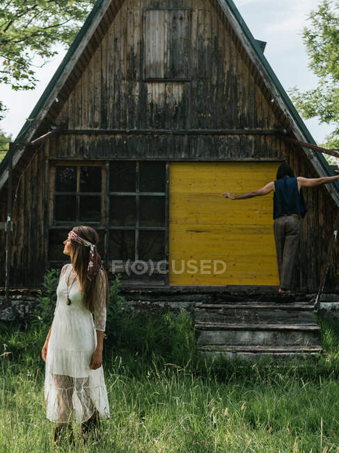 Close-up of a attractive girl looking away and in the background a man balancing on the porch of an abandoned wooden house — Stock Photo