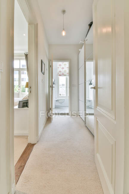 Estreito corredor vazio com roupeiro espelhado levando à sala de estar e banheiro no dia ensolarado no moderno apartamento espaçoso — Fotografia de Stock