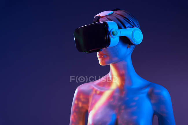 Maniquí femenino con auriculares VR de pie bajo brillante iluminación multicolor sobre fondo violeta - foto de stock
