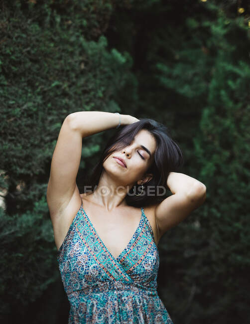 Vue de face d'une belle jeune femme les mains dans les cheveux dans un jardin tout en pensant les yeux fermés — Photo de stock
