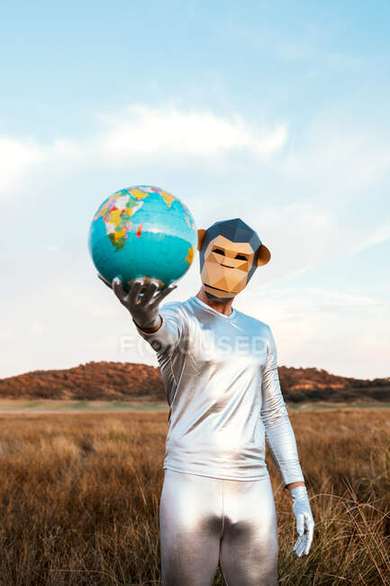 Анонімний хлопець у срібному латексному костюмі з геометричною мавпою дивиться на камеру і дарує глобус у природі — стокове фото