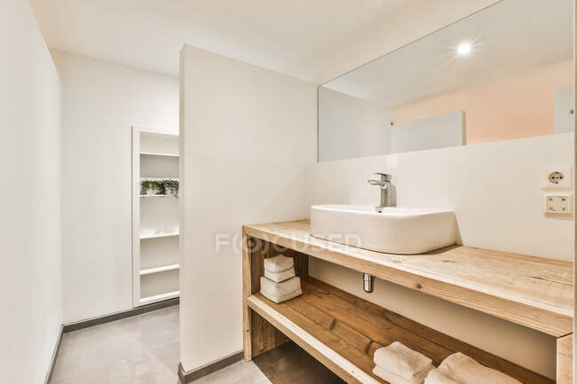 Design criativo do banheiro com lavatório entre espelho e prateleira de madeira com toalhas em casa com lâmpada brilhante — Fotografia de Stock