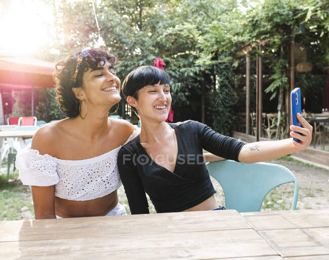 Contenido amigable hembras multirraciales tomando auto disparo en el teléfono móvil mientras disfrutan de fin de semana juntos en el parque de verano - foto de stock