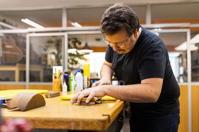 Konzentrierter Handwerker steht am Tisch und schleift Griffbrett der Gitarre in professioneller Werkstatt — Stockfoto