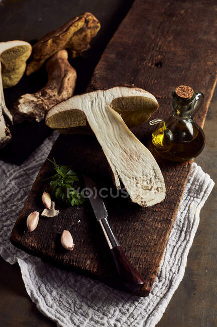 Вид сверху на сырые нарезанные грибы Boletus edulis на деревянной разделочной доске с чесноком и парслеем в легкой кухне во время приготовления — стоковое фото