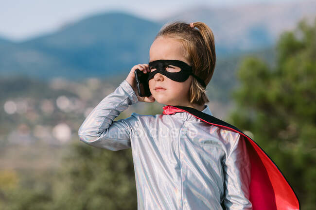 Fille auto assurée en costume de super-héros masque des yeux avec cape ayant appel téléphonique sur téléphone portable — Photo de stock
