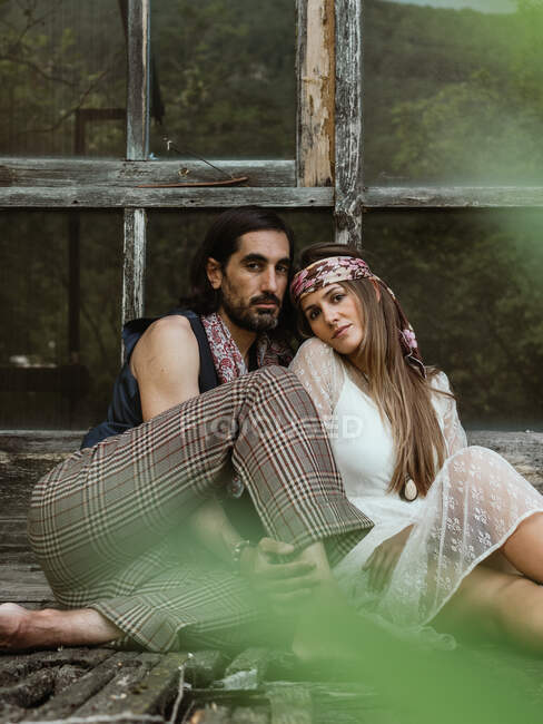 Vista frontal de um par de hippies abraçando no chão da varanda com os pés descalços — Fotografia de Stock