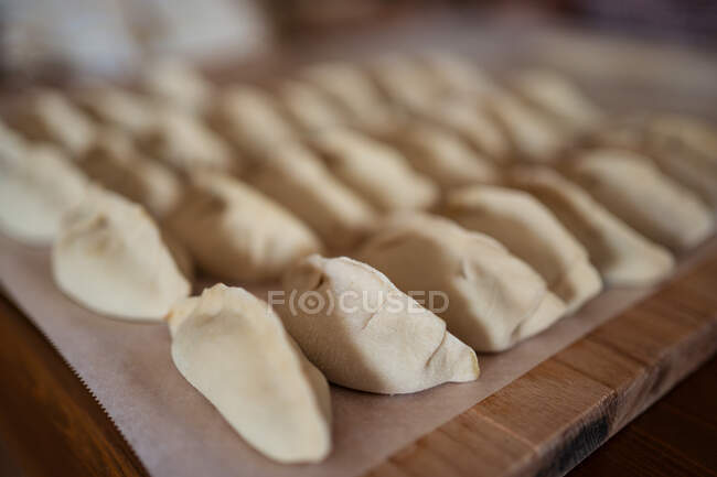 Closeup de bolinhos de jiaozi não cozidos recheados servidos em mesa de madeira em fileira na cozinha — Fotografia de Stock