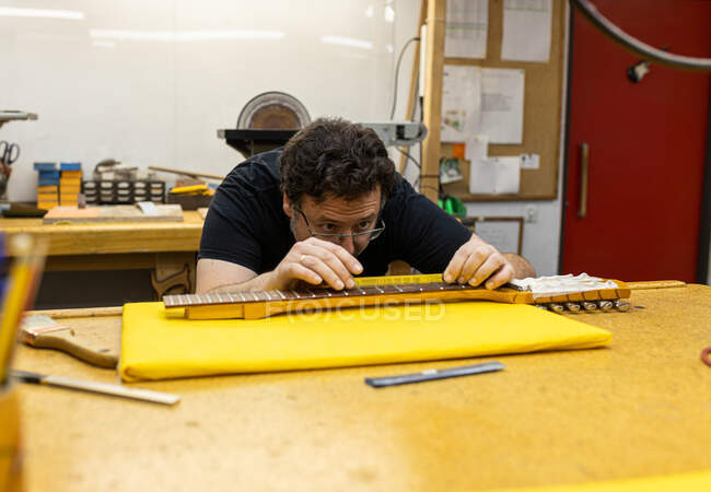 Konzentrierter Handwerker mit Brille, der den Abstand zwischen den Bünden am Gitarrenhals während der Arbeit im professionellen Studio misst — Stockfoto