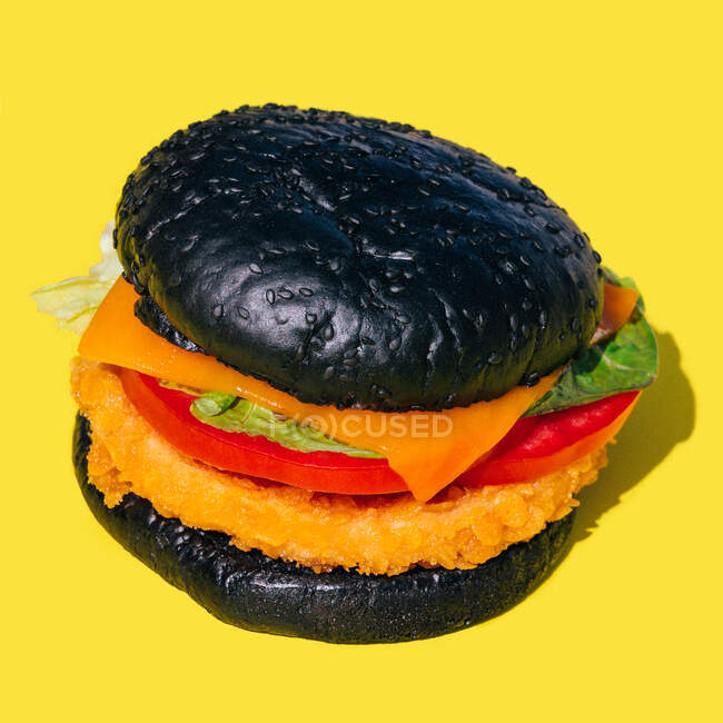 De arriba hamburguesa fresca con pan negro y verduras sobre fondo amarillo - foto de stock