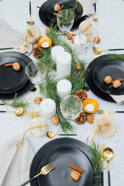 From above of table with dinnerware and cutlery near decorative fir branches and candles with walnuts and cinnamon sticks on plates — Stock Photo