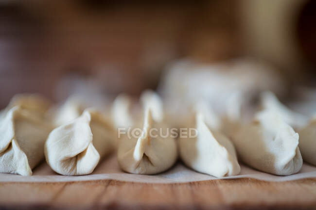 Closeup of stuffed uncooked jiaozi dumplings served on wooden table in row in kitchen — Stock Photo
