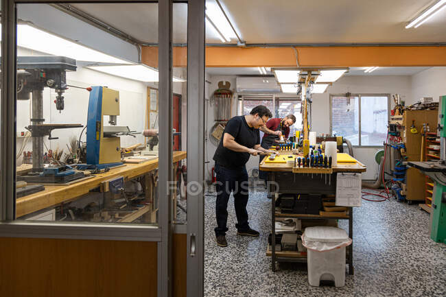 Специализированные мастера-лютиры, работающие в собственной мастерской по ремонту электрогитар с различным профессиональным оборудованием и стеклянными стенами — стоковое фото
