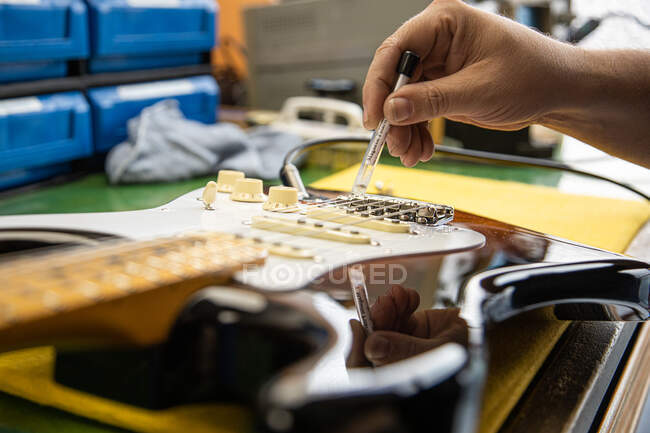 Crop anonymous male master setting up electric guitar bridge at table with various supplies with professional equipment in light workshop — Stock Photo
