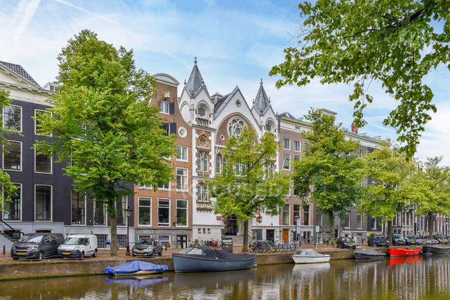 Classic church with windows and towers located on street with green trees near water canal with boats in Amsterdam city — Stock Photo