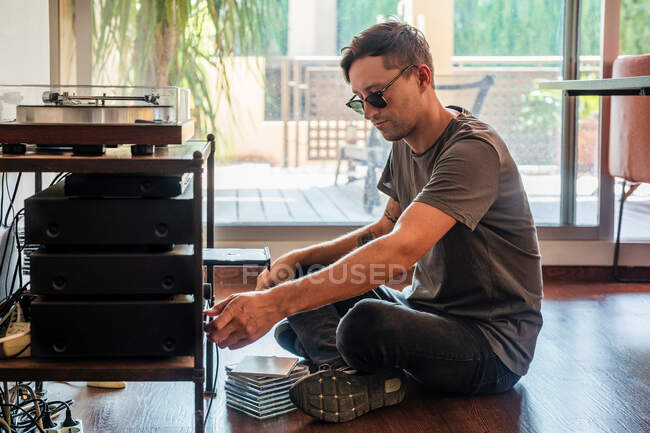 Seitenansicht eines Mannes, der Musik hört, während er in der Nähe des Spielers zu Hause auf dem Boden sitzt — Stockfoto