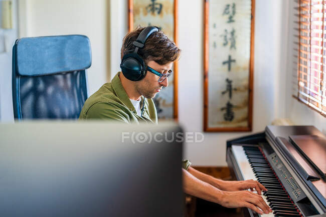Vue latérale d'un musicien en tenue décontractée jouant de la mélodie au piano assis dans un appartement moderne près d'une fenêtre — Photo de stock