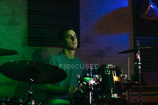 Jovem músico masculino concentrado tocando bateria no clube com iluminação de néon verde e azul — Fotografia de Stock