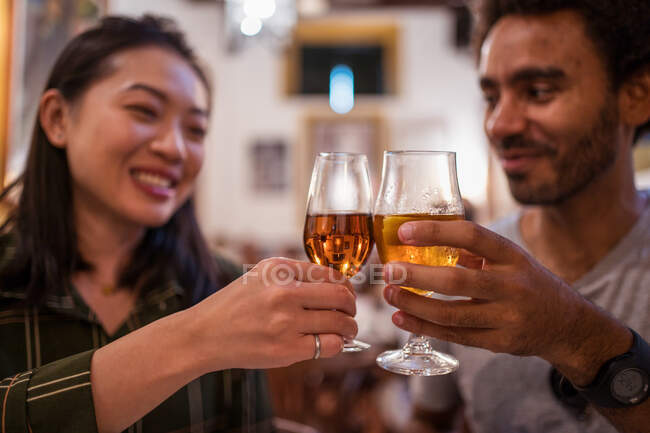 Weicher Fokus des multirassischen Paares, das während der festlichen Veranstaltung in einem modernen Restaurant zusammen zu Abend isst und Gläser mit Alkohol trinkt — Stockfoto