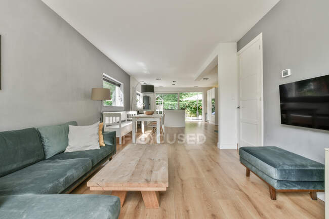 Gemütliche Couch in der Nähe von Holztisch in der Nähe Sessel gegen Wand mit Fernseher im hellen Wohnzimmer mit Fenster in der Wohnung — Stockfoto