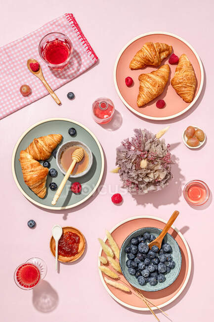 From above of composition of plated with fresh baked sweet croissants served with berries and jam placed on pink table — Stock Photo