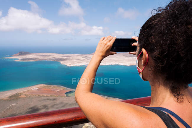 Back view of crop anonymous female tourist taking photo of Graciosa Island and Strait of Rio on cellphone in Spain — Stock Photo