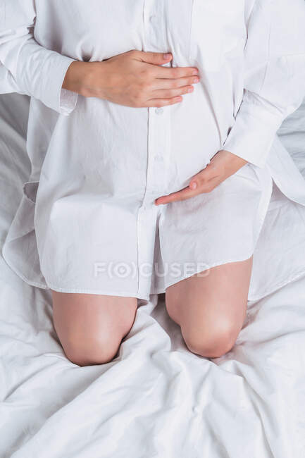 From above anonymous young pregnant gentle female touching tummy while sitting on bed — Stock Photo