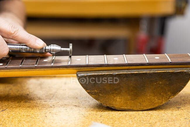 Crop anonymous master polishing frets on guitar neck with professional polishing wheel at table in light workshop on blurred background — Stock Photo