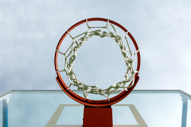 From below of round basketball hoop with white net attached to backboard against cloudy sky on playground in summer day — Stock Photo