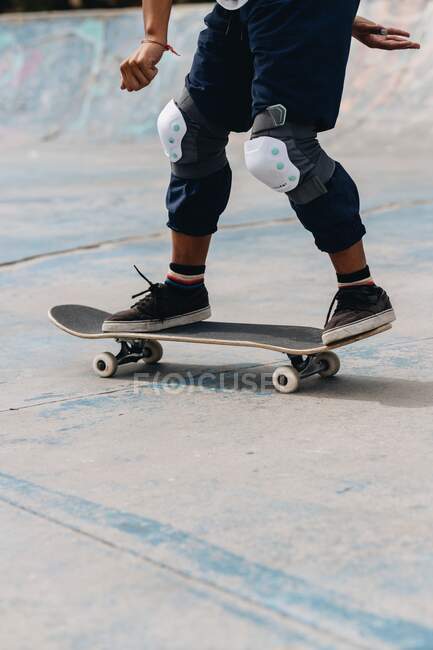 Anonyme junge ethnische Person in lässigem Outfit mit schützenden Knieschoner auf dem Skateboard im Skatepark — Stockfoto