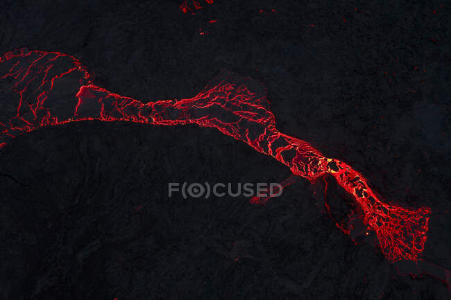 Vue de dessus du magma rouge chaud qui coule sur une surface montagneuse sombre la nuit dans les hautes terres d'Islande dans l'obscurité — Photo de stock