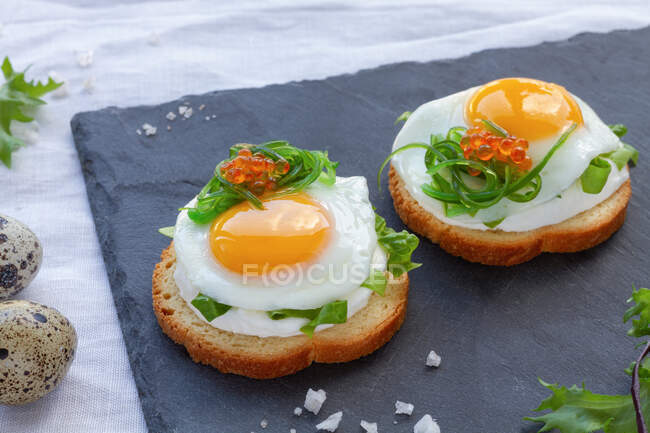 Dall'alto stuzzicanti tartine con pane croccante e uova di quaglia fritte decorate con erbe e caviale servite su tavola grigia — Foto stock
