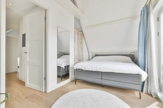 Komfortables Bad mit Decke in der Nähe des Fensters mit blauen Vorhängen im hellen Schlafzimmer mit Arbeitsbereich eingerichtet — Stockfoto