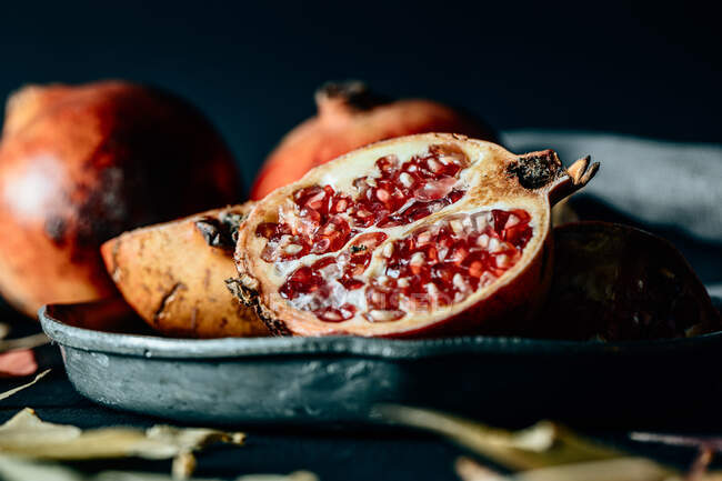 Halved and whole ripe pomegranate on frying pan placed on creased tablecloth on table — Stock Photo
