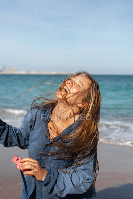 Щаслива жінка в мокрій сорочці, стоячи на піщаному пляжі біля моря, тримаючи фотоапарат в сонячний день — стокове фото
