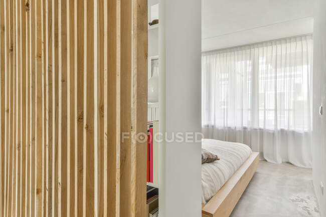 Zeitgenössische Schlafzimmereinrichtung mit Bett zwischen hölzerner Trennwand und Fenster mit Tüll im Leuchtturm — Stockfoto
