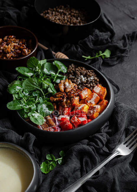 From above stewpan with lentils near salad with pumpkin and bell pepper decorated with green basil leaves on black background near salad dressing — Stock Photo