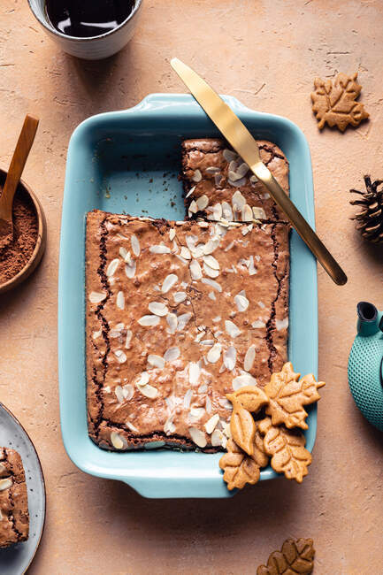 Draufsicht auf leckeren gebackenen Brownie mit Mandelflocken im Backblech mit Keksen auf dem Tisch mit Kakaopulver platziert — Stockfoto